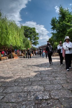 Yunnan, Çin. 30 Nisan 2024: Eski LiJiang kentindeki ünlü UNESCO antik kasaba mirasında turistlerin vitrinlere alışveriş yaptığı ve ticari mallar aradığı gündüz saatleri.