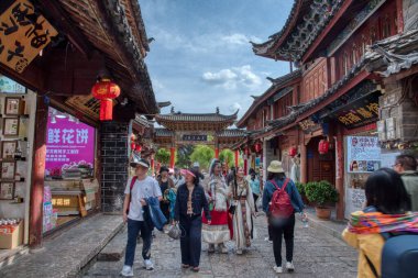 Yunnan, Çin. 30 Nisan 2024: Eski LiJiang kentindeki ünlü UNESCO antik kasaba mirasında turistlerin vitrinlere alışveriş yaptığı ve ticari mallar aradığı gündüz saatleri.