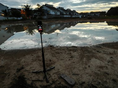 Perak,Malaysia. June 10,2024: Scene of capturing footage using Insta360 device at the pool of water during the dawn hour at Taman Permai Vacant plot of land. clipart