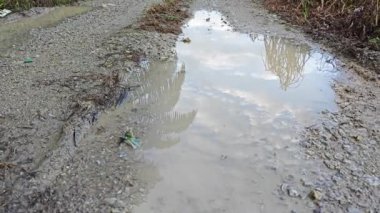 Kırsal toprak yolda sağanak yağış sonrasında durgun su havuzu yansıtıyor.   