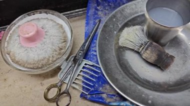 Yaşlı, kirli bir adamın tıraş fırçası, bir kase su, toz fırçası ve masanın üzerindeki hanım evladı..