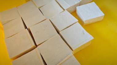 Kare şeklinde yumuşak, katı beyaz tofu blokları sarı plastik tepside..