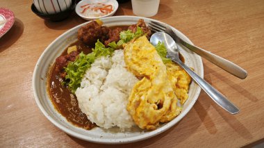 Bir tabak pilav sarılmış yumurta, sebze salatası ve Japon körili kızarmış tavuk eti. .  