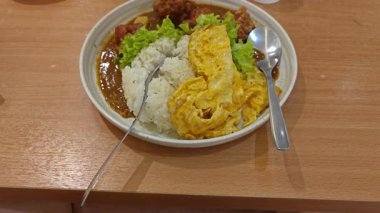 Bir tabak pilav sarılmış yumurta, sebze salatası ve Japon körili kızarmış tavuk eti.. 
