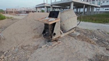 İnşaat alanındaki kum yığınının yanında eski bir çimento karıştırma makinesi..