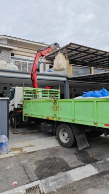 Perak, Malezya. 30 Mayıs 2025: Hooklift kamyon parkının manzarası çift katlı verandanın içinde yenileme malzemelerini Taman Mas 1, Kg koh 'un üst katındaki balkona taşıyor.. 