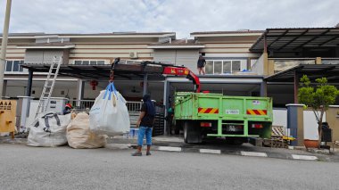 Perak, Malezya. 30 Mayıs 2025: Hooklift kamyon parkının manzarası çift katlı verandanın içinde yenileme malzemelerini Taman Mas 1, Kg koh 'un üst katındaki balkona taşıyor.. 