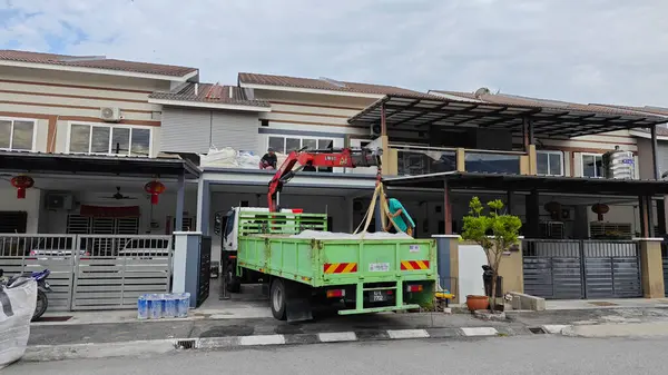 Perak, Malezya. 30 Mayıs 2025: Hooklift kamyon parkının manzarası çift katlı verandanın içinde yenileme malzemelerini Taman Mas 1, Kg koh 'un üst katındaki balkona taşıyor.. 