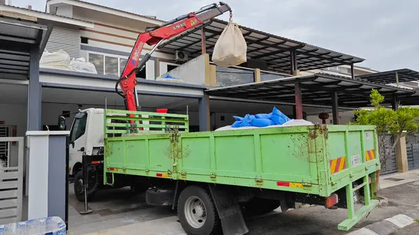 Perak, Malezya. 30 Mayıs 2025: Hooklift kamyon parkının manzarası çift katlı verandanın içinde yenileme malzemelerini Taman Mas 1, Kg koh 'un üst katındaki balkona taşıyor.. 