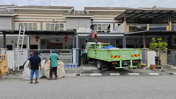 Perak, Malezya. 30 Mayıs 2025: Hooklift kamyon parkının manzarası çift katlı verandanın içinde yenileme malzemelerini Taman Mas 1, Kg koh 'un üst katındaki balkona taşıyor.. 