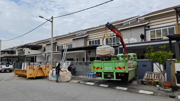Perak, Malezya. 30 Mayıs 2025: Hooklift kamyon parkının manzarası çift katlı verandanın içinde yenileme malzemelerini Taman Mas 1, Kg koh 'un üst katındaki balkona taşıyor.. 