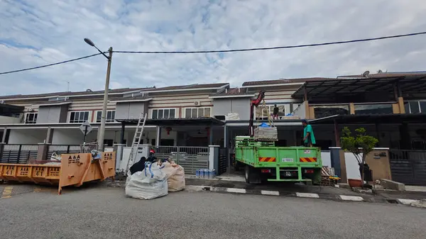 Perak, Malezya. 30 Mayıs 2025: Hooklift kamyon parkının manzarası çift katlı verandanın içinde yenileme malzemelerini Taman Mas 1, Kg koh 'un üst katındaki balkona taşıyor.. 