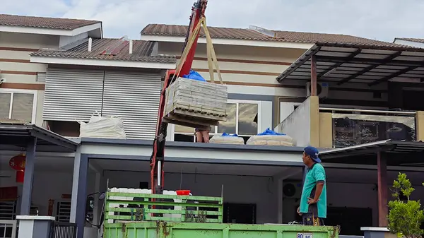Perak, Malezya. 30 Mayıs 2025: Hooklift kamyon parkının manzarası çift katlı verandanın içinde yenileme malzemelerini Taman Mas 1, Kg koh 'un üst katındaki balkona taşıyor.. 