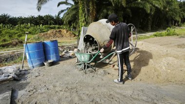 Perak, Malezya. 30 Mayıs 2025: Taman Indah Permai şantiyesindeki kum ve çimento torbalarının yanında çimento karıştırma makinesinde çalışan bir işçi.