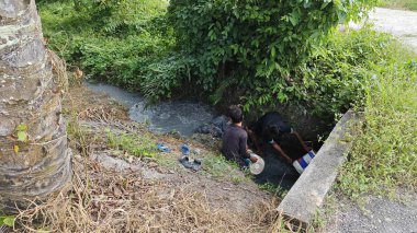 Perak, Malezya. 29 Mayıs 2025: Desa Permai Çiftliği 'nden akan suyun çamurunu yığarak bir drenaj tıkanıklığı yaparak tatlı su balığı yakalayan birkaç çocuğun sahnesi.