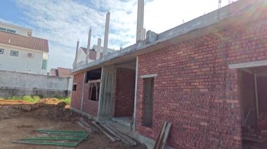 Perak, Malezya. 21 Haziran 2025: Taman Indah Permai şantiyesindeki inşaat duvarını inşa eden ve kapalı alanda çimento ve tuğla taşıyan işçilerin görüntüleri.