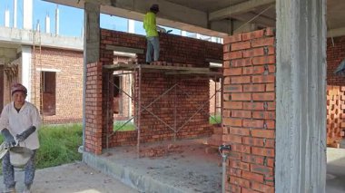 Perak, Malezya. 21 Haziran 2025: Taman Indah Permai şantiyesindeki inşaat duvarını inşa eden ve kapalı alanda çimento ve tuğla taşıyan işçilerin görüntüleri.