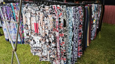 Perak, Malezya. 10 Temmuz 2025: Kg Koh perşembe pazarında indirimde ve sergilenmekte olan askılarda rengarenk giysiler bulunan güzel düzenlenmiş bir elbise rafı.