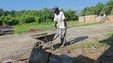 Perak, Malezya. 25 Temmuz 2025: Beton karıştırıcı üzerinde çalışan işçi, tramvayda çimento taşıyor, daha sonra kare şeklindeki metal kovayla halata döküyor ve Taman Permai Konut projesinde beton kaldırıyor, Kg Koh.