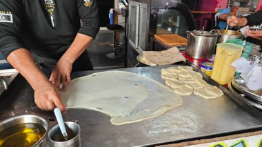 Perak, Malezya. 17 Ağustos 2025: Malezyalı bir sokak yemeği şefi, Roti Canai Sedap standında tavada ekmek pişirme konusundaki uzmanlığını gösteriyor, Kg Koh.