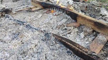 Çöp konteynırındaki kül yığınının etrafında yanan uzun bir odun parçası. 