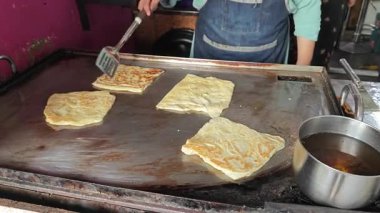 Perak, Malezya. 17 Ağustos 2025: Malezyalı bir sokak yemeği şefi, Roti Canai Sedap standında tavada ekmek pişirme konusundaki uzmanlığını gösteriyor, Kg Koh. 