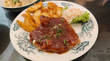 Baharatlı soslu bir tabak kızarmış tavuk pirzolası dilimlenmiş patates ve lahana mayonezi..