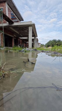 Bitmemiş inşaat binasının etrafında toplanan durgun yağmur suyu havuzu.