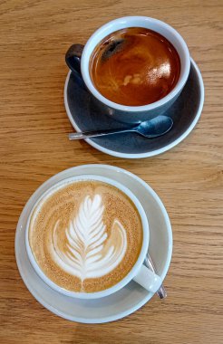 iki bardak kapuçino, latte sanat ve sade kahve ahşap bir masada.