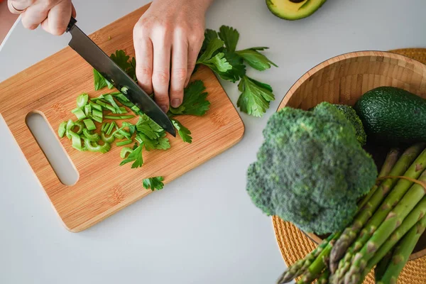 stock image The process of cutting celery on the wooden cutting board. Cooking of the healthy food. Bright green celery, broccoli, asparagus and avocado close up