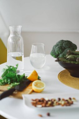 Sağlıklı gıda konsepti. Meyveler, fındıklar ve sebzeler mutfakta. Fındık, limon, salata, kuşkonmaz ve brokoli beyaz masada pişmeyi bekliyor. Sağlıklı yemek hazırlıyorum. Vejetaryen yemeği