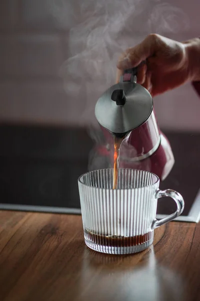 stock image Woman pouring hot coffee from moka pot into the glass. Aroma beverage in the morning. Tasty breakfast. Hot coffee with steam