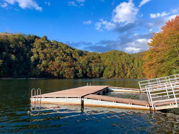 Wooden pontoon on a lake surrounded by forest turning yellow on a sunny autumn day with clear blue sky