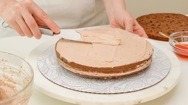 Assembling the cake. Woman hands topping part of the cake with chocolate cream. Step by step chocolate cake recipe, close up baking process