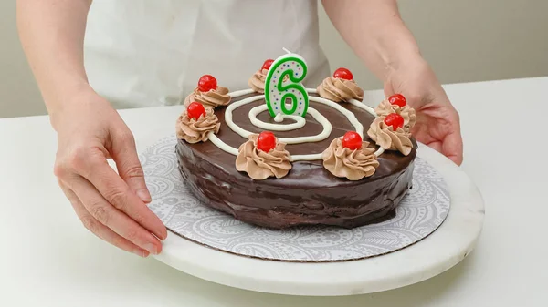 Woman decorating cake with candle in the form of number Six. Homemade cake decorated with chocolate cream and cherries close up