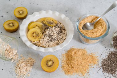 Tam tahıllı yulaf, keten tohumu, çim tohumundan yapılmış bir tabak yulaf ezmesi ve açık gri taştan arka planda sergilenen tatlı altın kivi ile servis edilir.