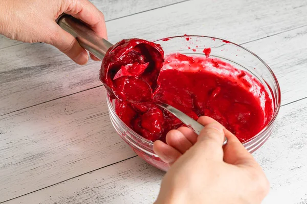 Blending cranberry sauce, making it extra-smooth. Bowl of fresh cooked homemade cranberry sauce close-up on kitchen table, woman hands