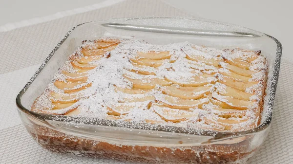 Fresh baked apple cake with biscuit base close up on kitchen table, just from the oven. Topping cake with powdered sugar.