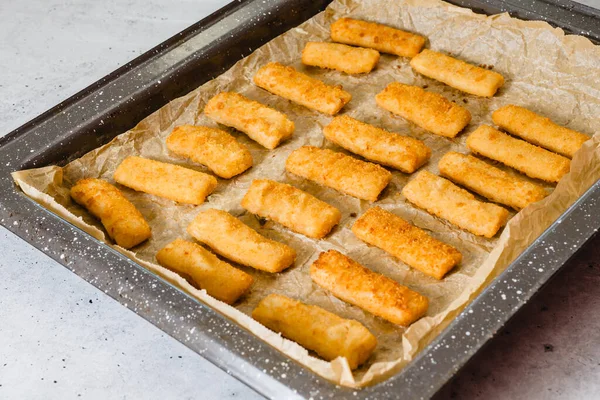 Baking pan with fish sticks close up on the kitchen table. Crunchy delicious lightly breaded with panko bread crumbs fish sticks