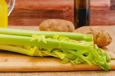 Kereviz sapı ve patatesler tahtaya yakın çekim. Çiğ sebze ve zeytinyağı. Kereviz çorbası tarifi için gerekli malzemeler