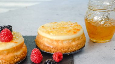 Mini cheesecake 'ler yakın plan. Portakal reçelli peynirli kekler, taze böğürtlenler ve biberiye, yakın plan dekorasyon süreci.