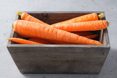 Carrots in a wooden box close-up on a light grey stone background, copy space
