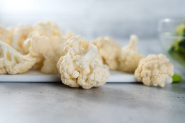 Cauliflower florets close-up on cutting board on a light grey stone background, copy space