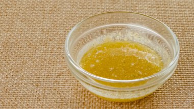 Mix of melted butter and garlic seasoning close-up in a glass bowl on a kitchen table in rustic background, copy space