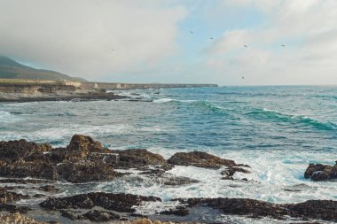 Rocky cliffs on the beach and turquoise colored sea waves, California Central Coast
