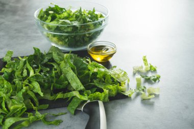 Cut fresh romaine lettuce close-up in a glass bowl and on a cutting board on a grey stone background, copy space