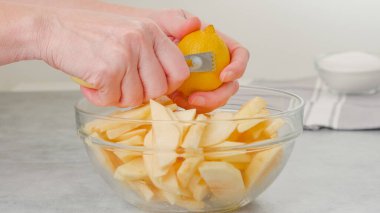 Woman hands topping apple slices with lemon zest using a citrus zester, apple cake recipe