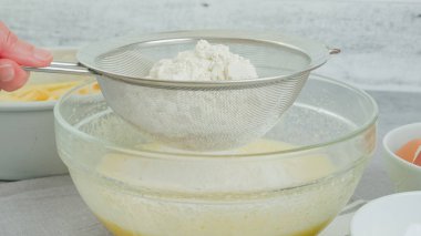 Cake dough preparation process. Chef pouring or sifting flour in a glass bowl using a colander. Homemade apple cake recipe, close-up view, woman hands