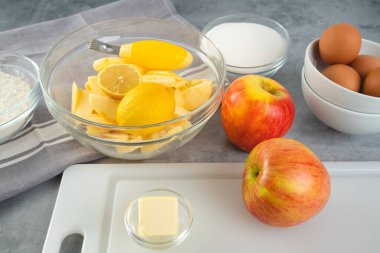 Baking pan with apple slices, lemon, eggs, sugar, and flour in bowls close-up on a kitchen table. Apple cake recipe, preparation process