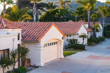 Beautiful houses with nicely landscaped front the yard, and green hills and clear blue sky in the background in a small beach town in California at sunset